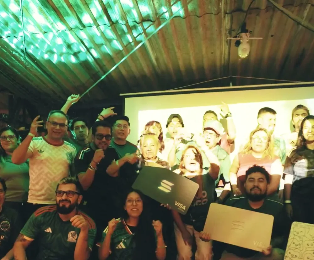 Fans in Mexico shirts holding giant KAST cards at a World Cup watch party in Mexico