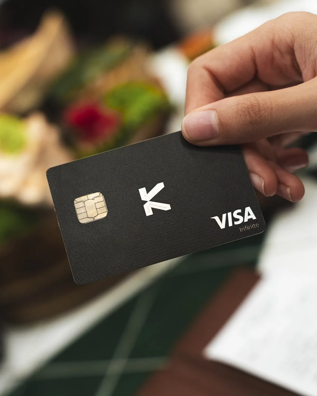 Hand holding a black KAST Visa card at dinner