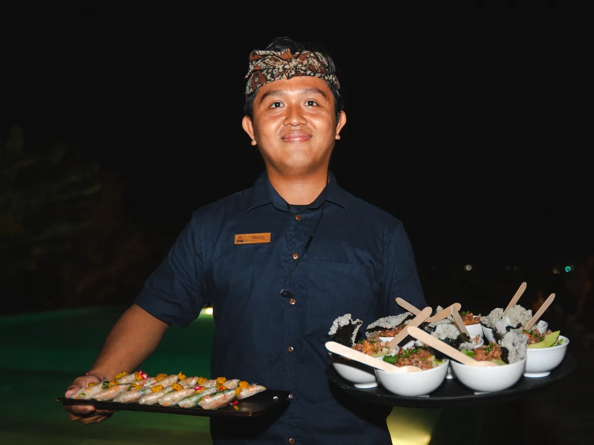 Waiter in a Balinese udeng serving food at a restaurant in Bali