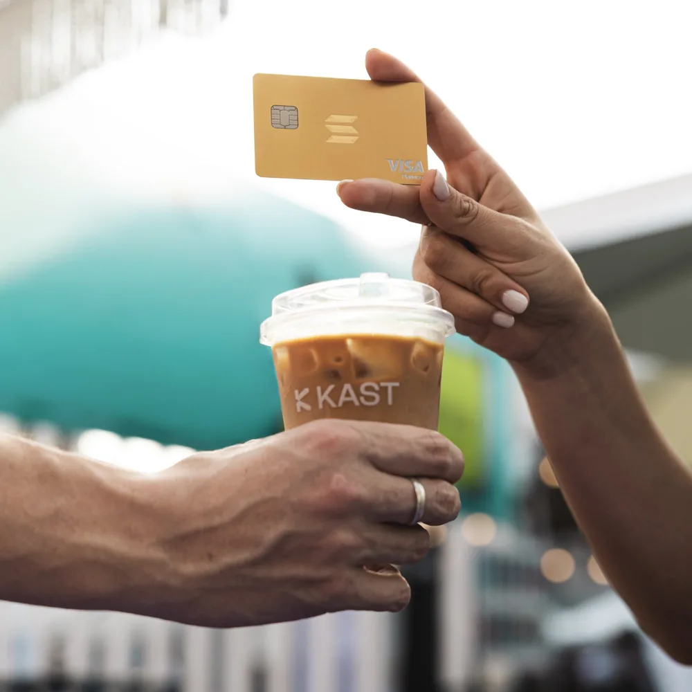 KAST Solana Gold card handed over with a KAST iced coffee