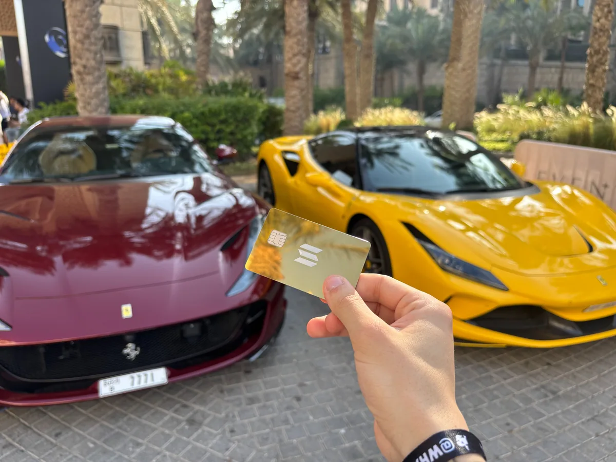 Gold KAST Solana card in front of Ferrari sports cars in Dubai