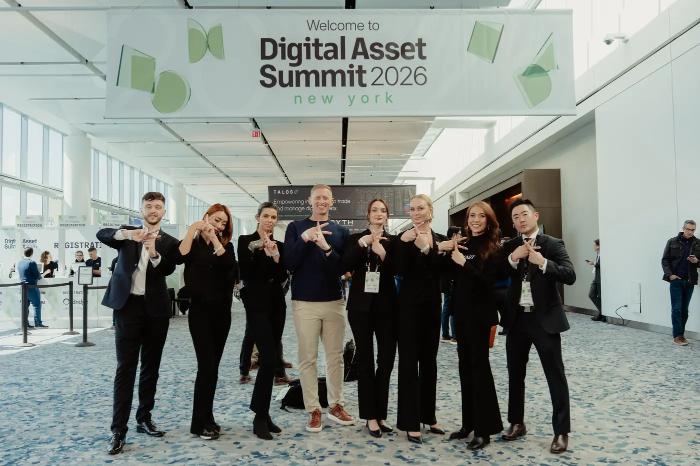 Group making the KAST K hand sign under the Digital Asset Summit 2026 New York welcome banner
